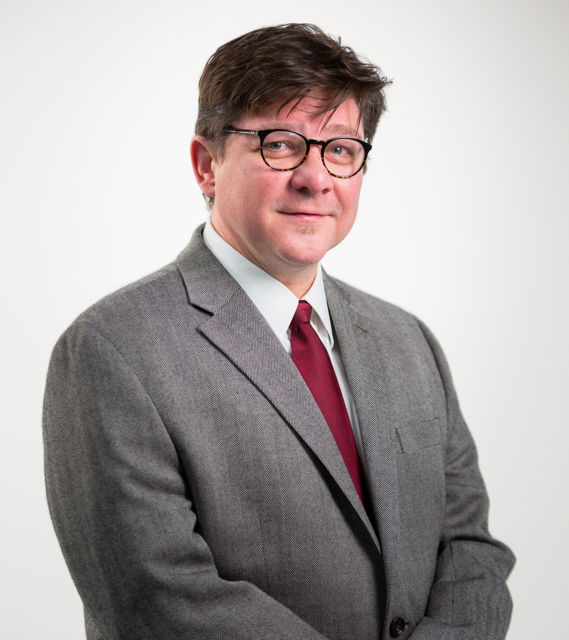 Male portrait of Board member Chris wearing grey suit and red tie
