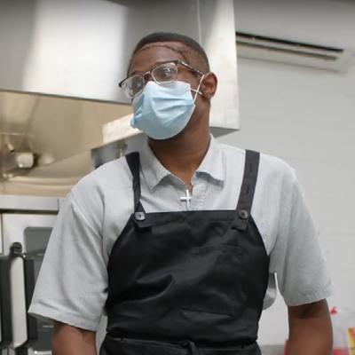 Picture of male in commercial kitchen wearing a black apron face covering.